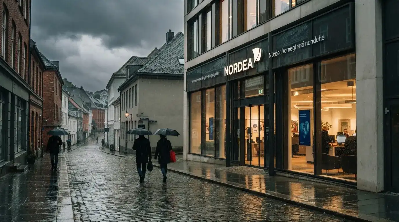 Bankfilial med store vinduer i en norsk by i regnvær, noen med paraplyer utenfor